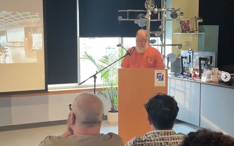 David Milley standing behind a podium, reading a poem.